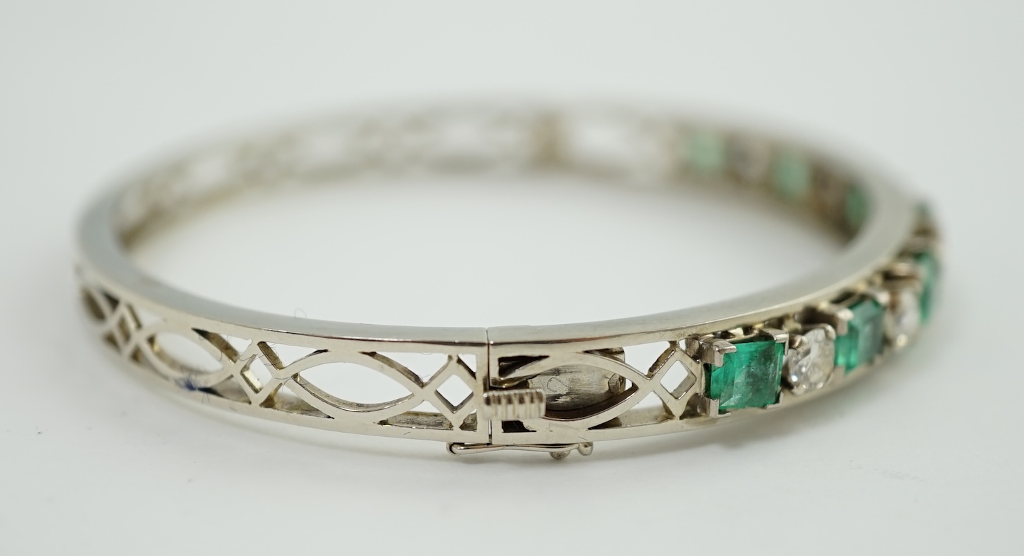 A modern 14k white gold, seven stone graduated emerald and six stone round cut diamond set hinged bangle